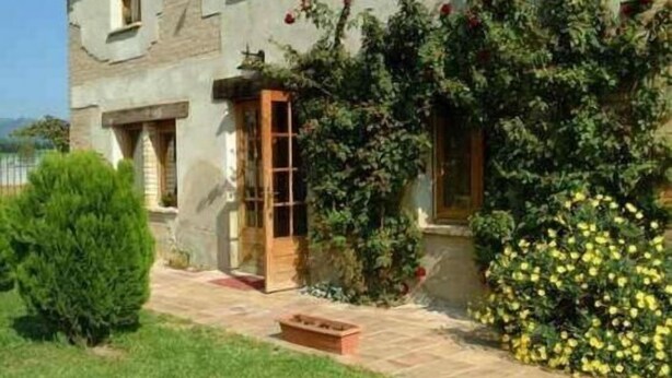 A stone building with a wooden door and windows, surrounded by greenery and a small garden. - Self catering Can Salvà for 12 people (Vilobí d'Onyar)
