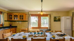 A cozy kitchen with wooden cabinets, a dining table set with cups and saucers, and a view of the outdoors through a window. - Self catering Can Salvà for 12 people (Vilobí d'Onyar)