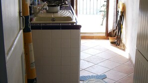 Una cucina con pavimento piastrellato, lavello e finestra che dà su un balcone.