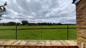 A view from a balcony overlooking a grassy field with a brick wall on one side. - Meadow View | Witney Holiday Let | 1 Bed & Sleeps 2 (Witney)