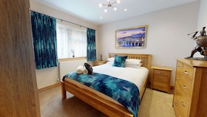 A bedroom with a wooden bed, a nightstand, a dresser, and a cityscape painting on the wall. - Meadow View | Witney Holiday Let | 1 Bed & Sleeps 2 (Witney)