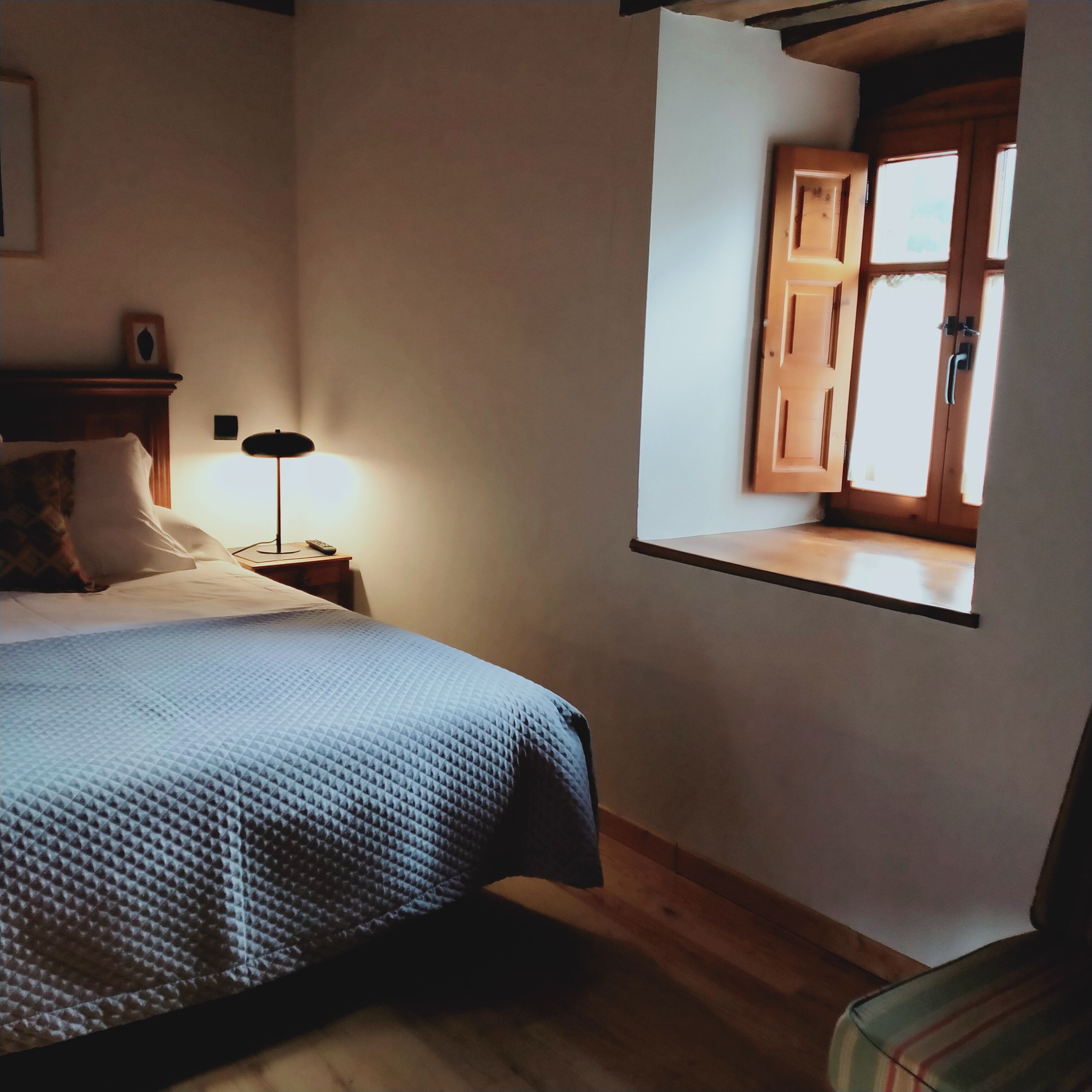 A bedroom with a bed, a nightstand, a lamp, and a window with wooden shutters.