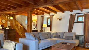 A cozy living room with a wooden ceiling, a grey sectional sofa, a wooden coffee table, and a staircase leading to another level. - The Abode of Vadinia (Burón)