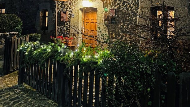 A stone building with a wooden balcony adorned with greenery and lights, suggesting a cozy, rustic setting. - The Abode of Vadinia (Burón)