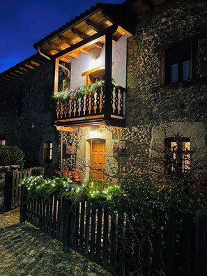 Ein Steinhaus mit einem hölzernen Balkon, der mit Grünpflanzen und Lichtern geschmückt ist und eine gemütliche, rustikale Atmosphäre ausstrahlt.
