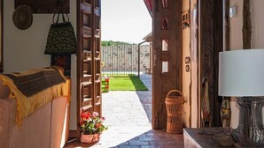Eine offene Tür führt zu einer Terrasse mit Steinboden, einem Korbwäscheschrank und einem kleinen Garten mit Blumen.