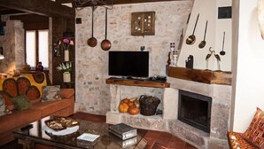 Ein gemütliches Wohnzimmer mit Kamin aus Stein, einem Flachbildfernseher und einer Holzbalkendecke.