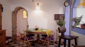 Un'area pranzo con un arco in pietra, un tavolo rotondo apparecchiato con piatti e bicchieri, e una sveglia appesa al muro.