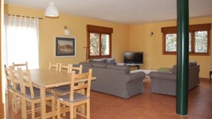 Een woonkamer met een zithoek, een televisie en een eettafel met stoelen.