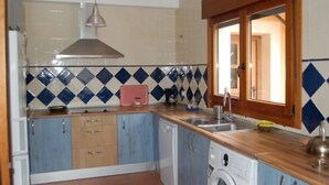 Een kleine keuken met een betegelde spatwand, houten kastjes, een ingebouwde vaatwasser en een raam met houten kader.