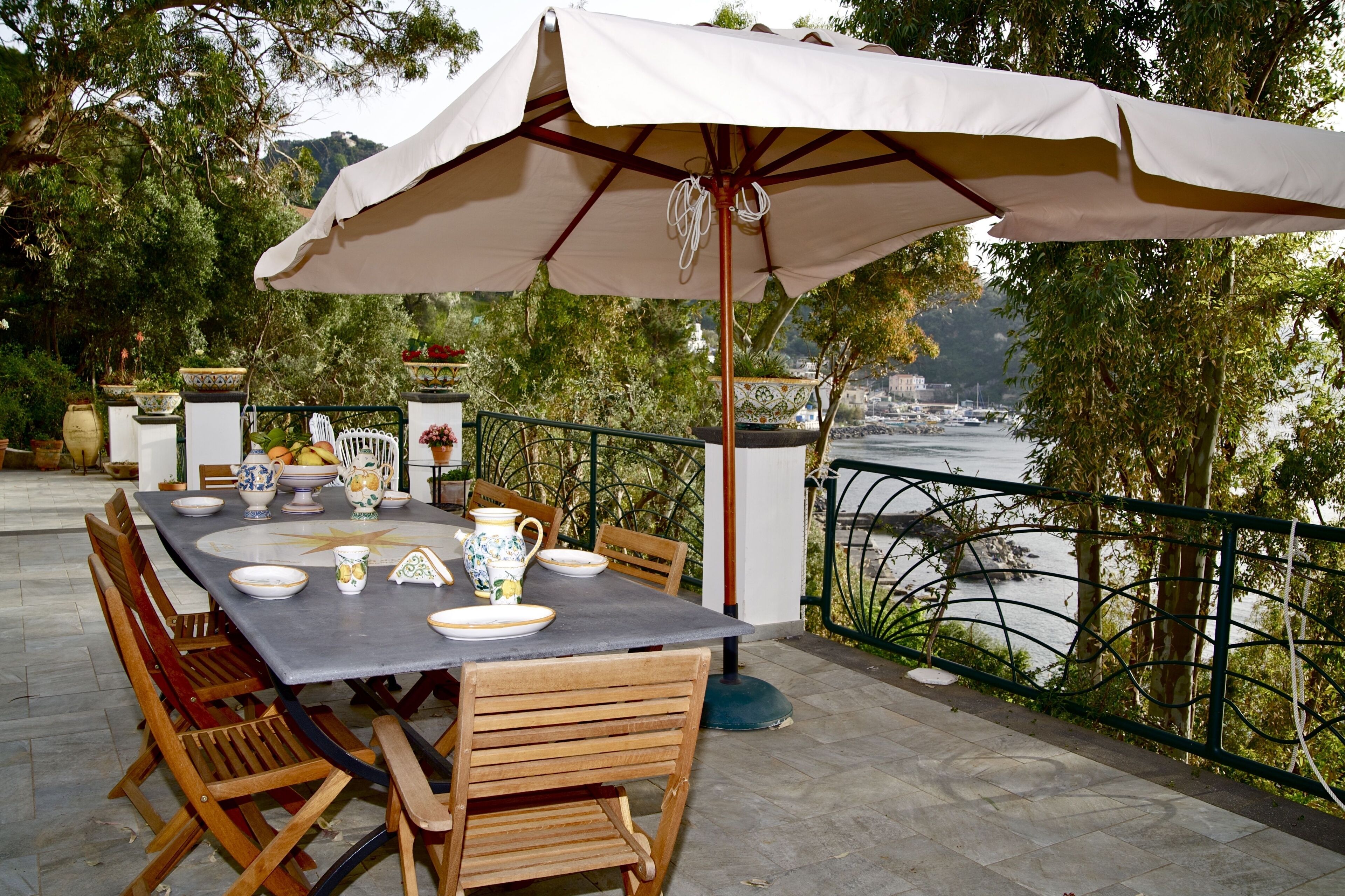 Un área de comedor al aire libre con una mesa dispuesta para cuatro personas, rodeada de sillas de madera, bajo un paraguas grande.
