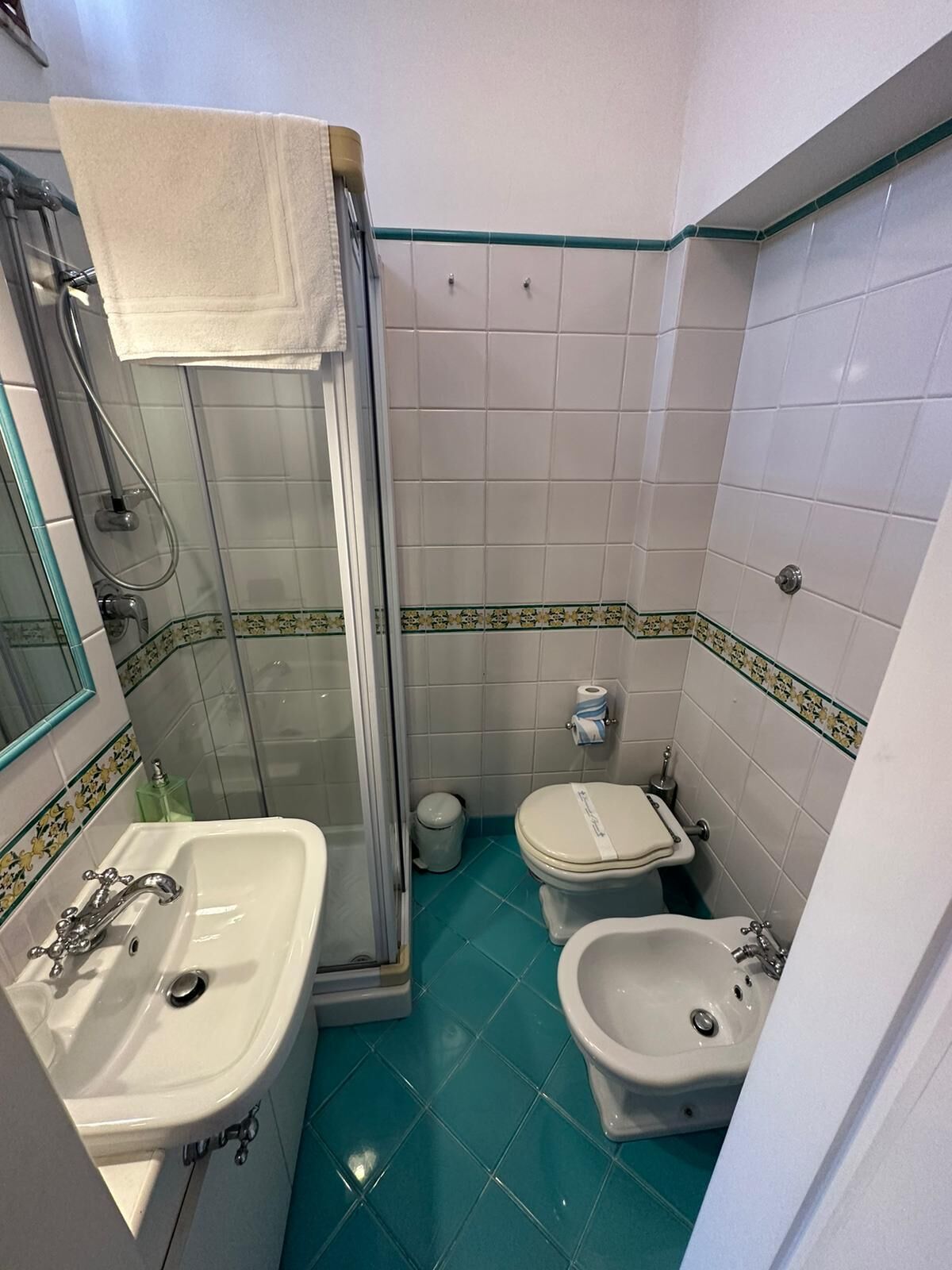 A small bathroom with a shower, two toilets, a sink, and a bidet.