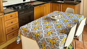 Een keuken met houten kastjes, een gasfornuis, een magnetron en een tafel met een tafelkleed met bloemen.