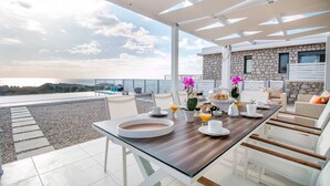 Una terrazza con tavolo apparecchiato per la colazione, con vista su una piscina e un edificio in pietra.