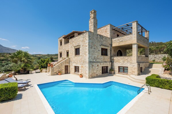 A stone villa with a swimming pool, outdoor seating, and a view of the surrounding landscape.