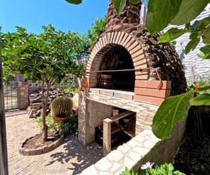 An outdoor brick oven with a stone base, surrounded by greenery and a small tree. - "Purple House" Sea View Apartments in Cala gonone (Dorgali)