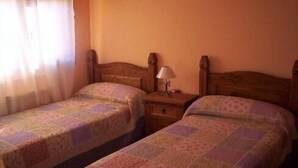 Une chambre avec deux lits en bois, une table de chevet avec une lampe et une fenêtre avec des rideaux.