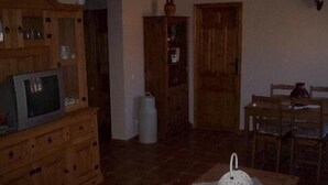 Un salon comprenant un meuble en bois, un téléviseur, une table à manger avec des chaises et une porte.