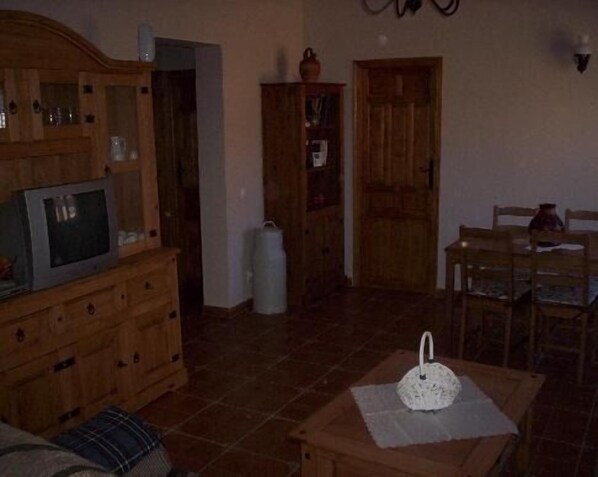 Ein Wohnzimmer mit einem Holzkabinett, einem Fernseher, einem Esstisch mit Stühlen und einer Tür.