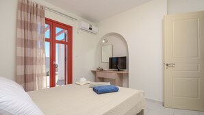 A hotel room with a bed, a desk with a computer, a TV, and a door. - DUNES Villa with Private pool for 6 (Naxos)