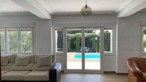 A spacious living room with a beige sofa, a brown leather chair, and a large sliding glass door leading to a pool. - Tranquility, calm and relax. (Olite)