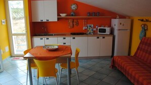 A compact kitchen with a dining table and chairs, a refrigerator, and a microwave. - Apartment Lumia Bilo Mansard at the sea (Sciacca)