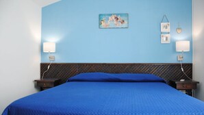 A room with a large bed, two bedside tables, a headboard with a patterned design, a wall-mounted picture, and two wall-mounted lamps. - Apartment Lumia Bilo Mansard at the sea (Sciacca)