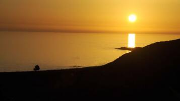 A sunset over a calm sea with a silhouette of a person and a small island.