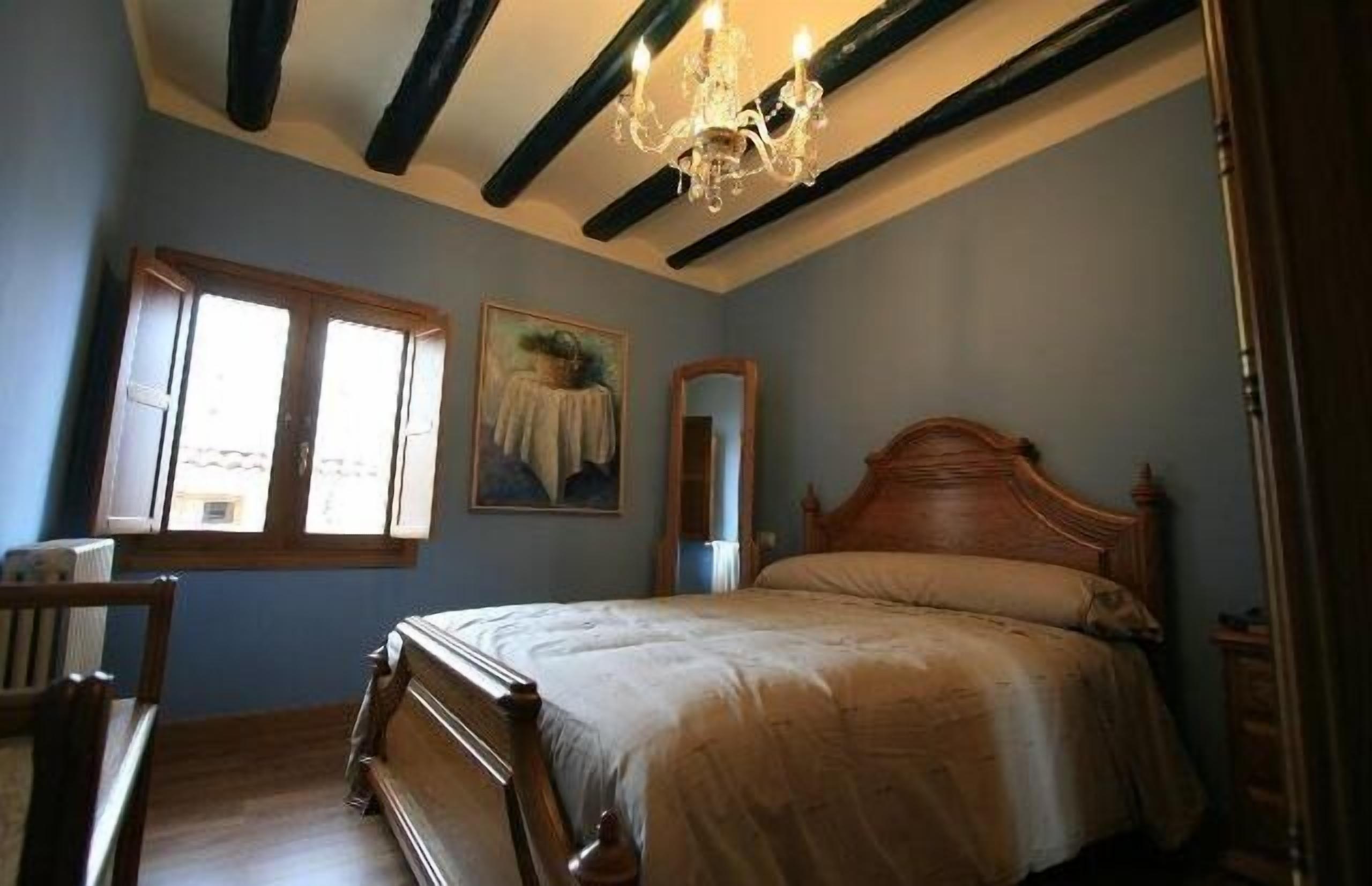 Une chambre à coucher avec un lit en bois, un lustre, une fenêtre avec des volets et un tableau au mur.