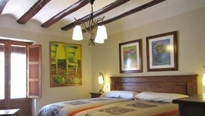 Una camera da letto con soffitto in legno, un letto con copriletto decorato, due quadri appesi alla parete e un comodino con una lampada.