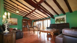 Un ampio soggiorno con pavimento in legno, soffitto alto con travi a vista, camino e zona pranzo con sedie e tavolo.