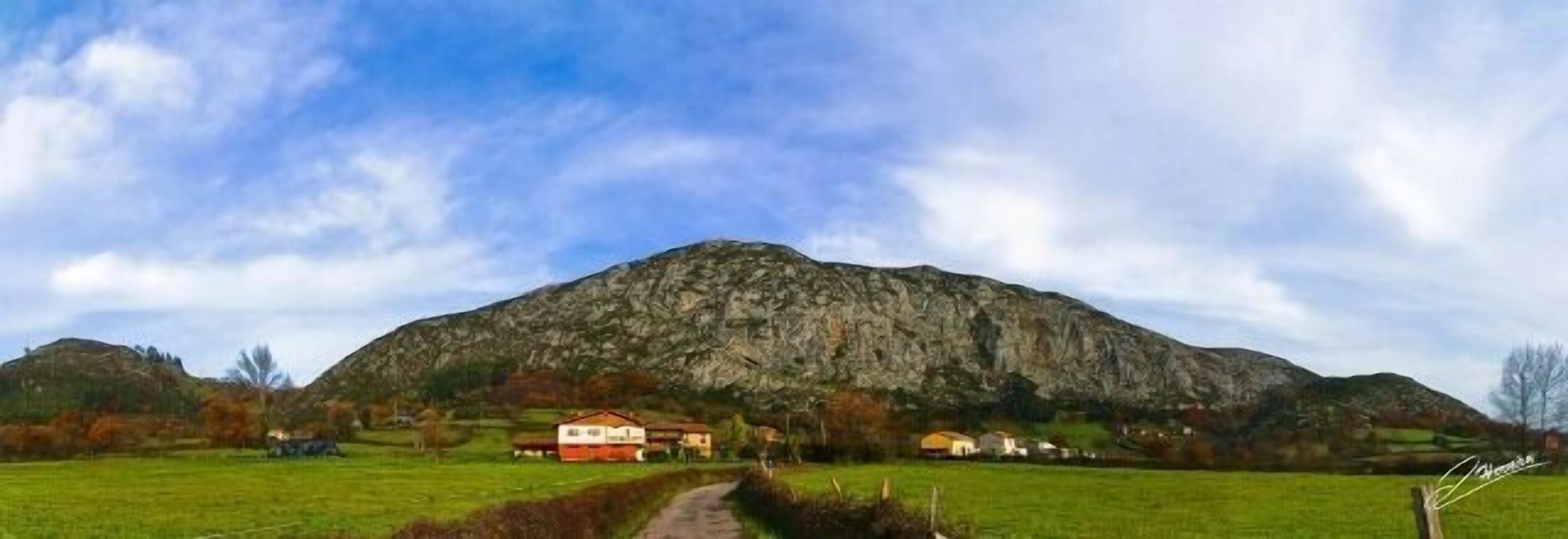 A rural landscape with a prominent mountain, a path leading to a cluster of houses, and a clear sky.