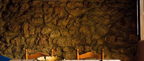 Uma mesa com toalha xadrez, duas cadeiras de madeira e uma parede de pedra com um quadro emoldurado acima.