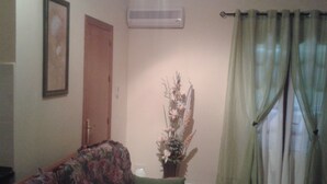 Een woonkamer met een bloemenbank, een groene kussen, een plant in pot en een deur.