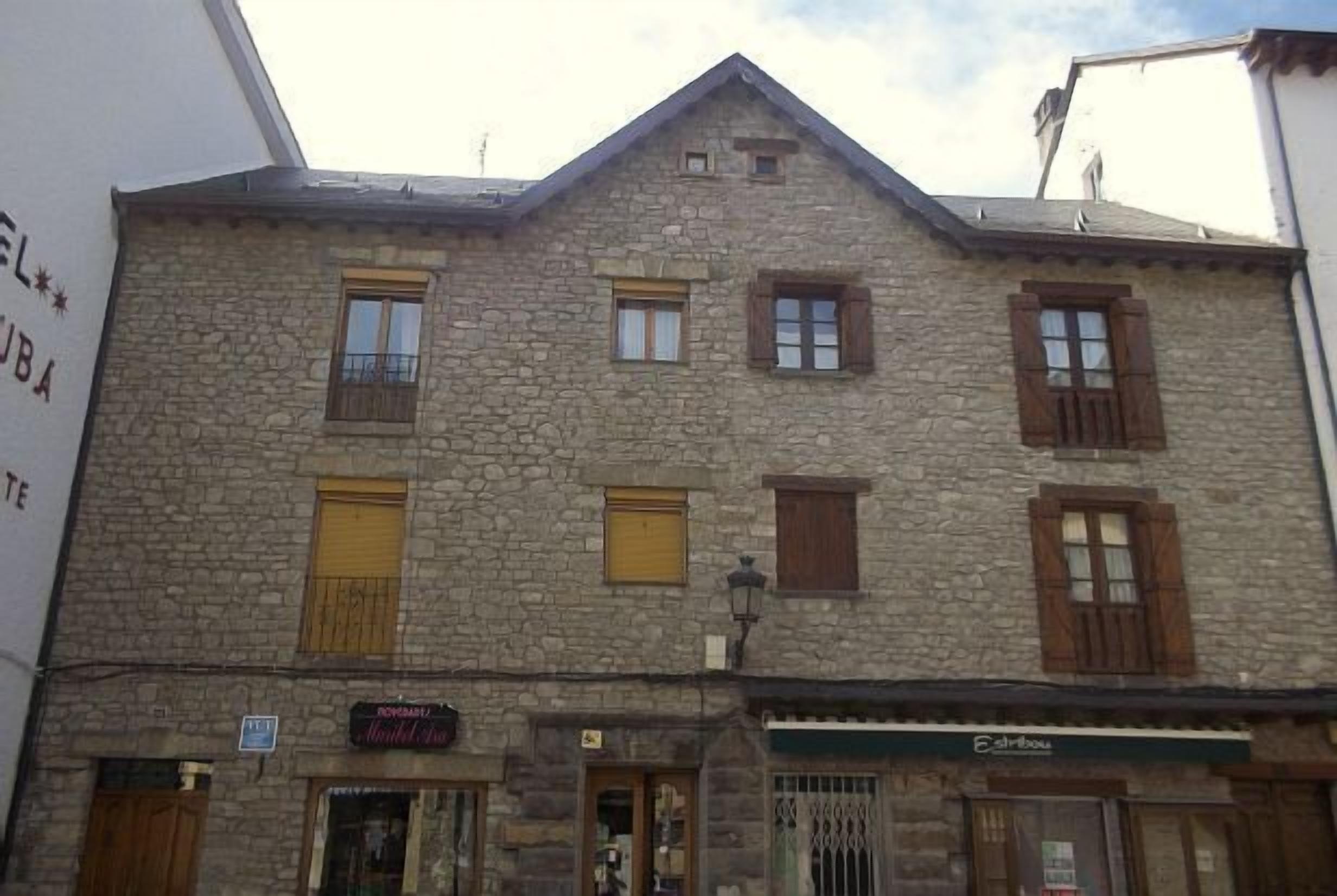 A stone building with multiple windows and doors, some with shutters. There are signs for a restaurant and a shop on the ground floor.