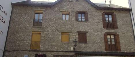 A stone building with multiple windows and doors, some with shutters. There are signs for a restaurant and a shop on the ground floor.