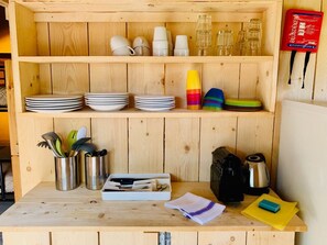 A wooden kitchen counter with stacked plates, cups, and a coffee maker. - LODGE TENT MARGHERITA 5 p. Glamping in Tuscany (Montescudaio)