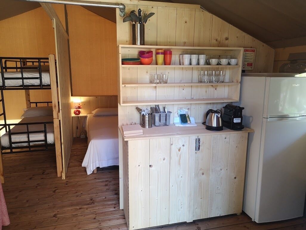 A compact kitchen with wooden cabinets, a white refrigerator, and a sink. There are shelves above the sink holding various kitchen items.