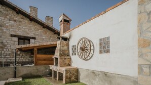 Un edificio de piedra con una chimenea de ladrillo, una pérgola de madera y una rueda decorativa en la pared.