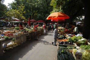 Ein Markt im Freien mit verschiedenen Ständen, an denen frische Lebensmittel unter roten Sonnenschirmen verkauft werden.