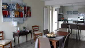 A dining area with a wooden table and chairs, a kitchen in the background, and a large abstract painting on the wall. - "Les Rousserolles"- Between LAC du BOURGET and CHAMBERY, T 2 (64m2), 3 stars NN (La Motte-Servolex)