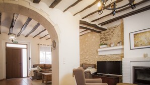 Ein Wohnzimmer mit Kamin, Steinwand und Holzbalken. Ein Fernseher und ein Sofa sind ebenfalls vorhanden.
