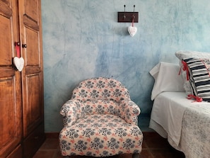 Une pièce comprenant un fauteuil à motifs floraux, une armoire en bois et un lit avec un oreiller à rayures.