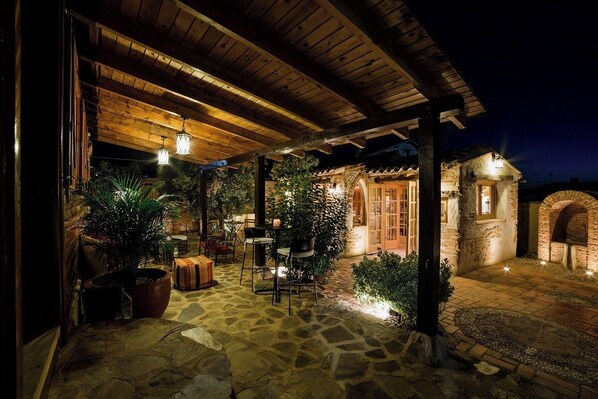 An outdoor patio area with stone flooring, wooden pergola, and potted plants.