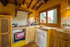 Une cuisine compacte avec un mur en briques, des poutres en bois, un lave-linge et une fenêtre donnant sur un beau paysage.
