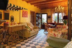 A cozy living room with a checkered floor, a wooden desk, a sofa, a chair, and a bookshelf.