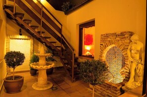 A staircase leading to an upper level, a stone wall with a mosaic, and a statue.