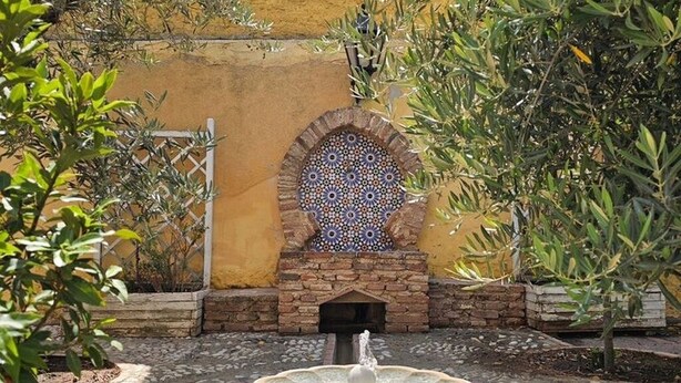 Un cortile con una fontana, un muro decorativo e vegetazione circostante.