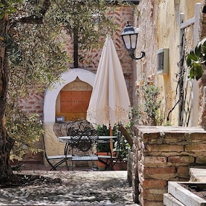 An outdoor seating area with stone walls, a wooden door, and a table with a white umbrella.