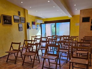 A room with multiple wooden chairs arranged for seating, a tiled floor, and a large window providing natural light.